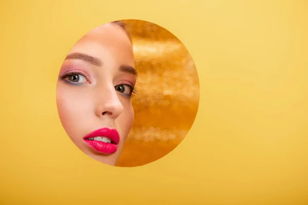 Belle femme avec un maquillage coloré regardant à travers le trou de cercle en papier jaune — Photo de stock