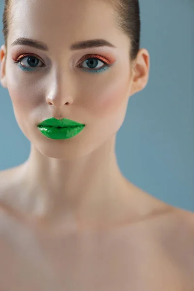 Retrato de hermosa mujer desnuda con labios verdes, sombra de ojos rosa y azul aislado en azul - foto de stock