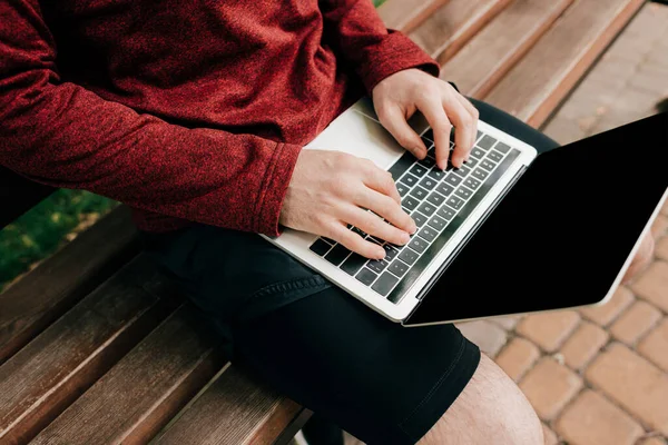 Cropped view of teleworker using laptop on bench on urban street — Stock Photo