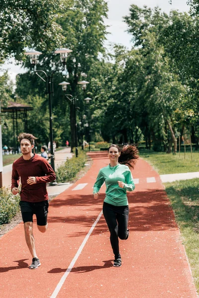 Красивий чоловік біжить біля позитивної дівчини на біговому шляху в парку — стокове фото