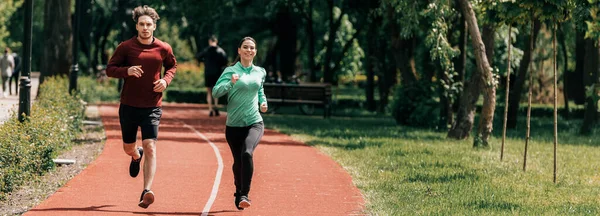 Панорамний знімок усміхненої жінки біжить біля хлопця на біговій доріжці в парку — стокове фото