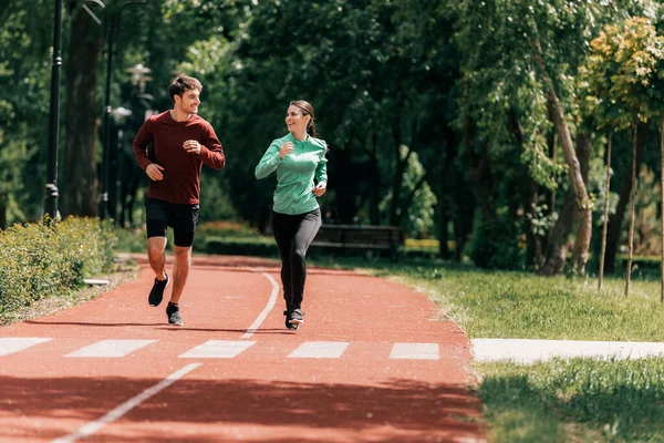 Couple souriant tout en faisant du jogging sur la piste de course dans le parc — Photo de stock