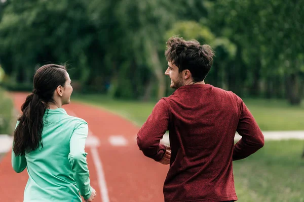 Back view of man smiling at girlfriend while running in park — Stock Photo