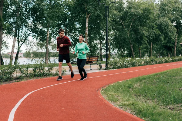 Jeune couple souriant courant ensemble sur le sentier de course dans le parc — Photo de stock