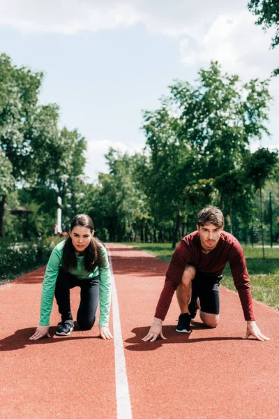 Pareja joven en posición inicial en pista de atletismo en parque - foto de stock