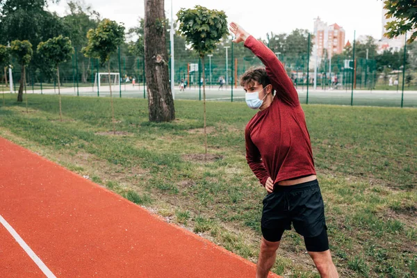 Esportista em máscara médica exercitando-se na pista no parque — Fotografia de Stock
