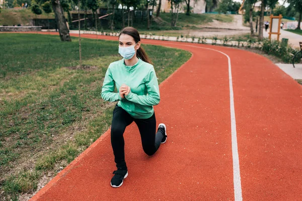 Спортсменка в медичній масці робить легені під час роботи в парку — стокове фото