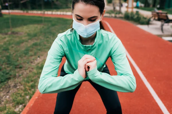 Sportswoman in medical mask exercising on running track in park — Stock Photo