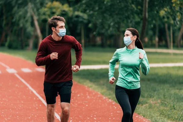 Молода пара в медичних масках біжить по біговій доріжці в парку — стокове фото