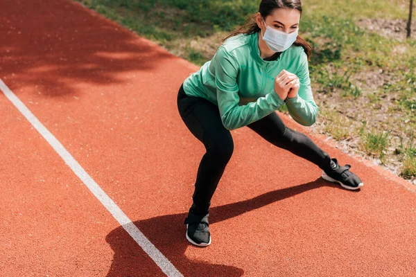 Спортсменка в медичній масці робить легені на треку в парку — стокове фото