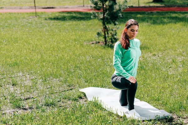 Deportiva haciendo ejercicio en la alfombra de fitness en la hierba en el parque - foto de stock