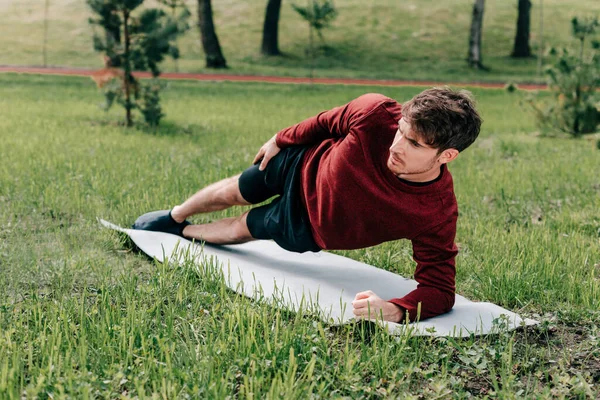Красивый спортсмен делает боковую доску на фитнес-коврике в парке — стоковое фото