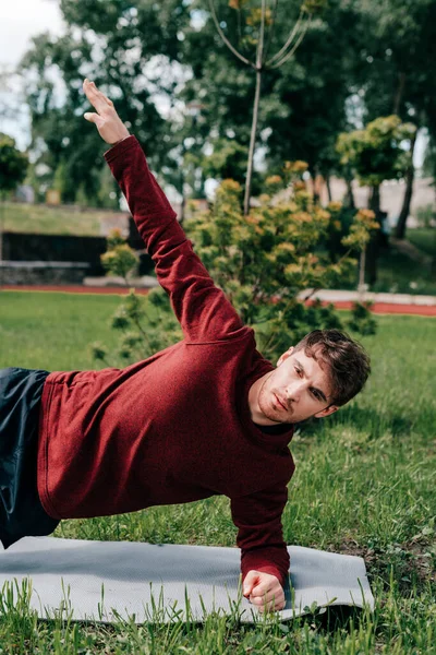 Hombre guapo haciendo tablón lateral mientras hace ejercicio en la alfombra de fitness en el parque - foto de stock