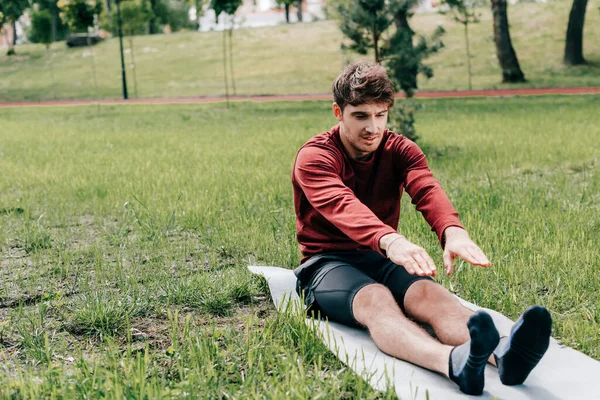 Handsome sportsman warming out on fitness mat in park — Stock Photo