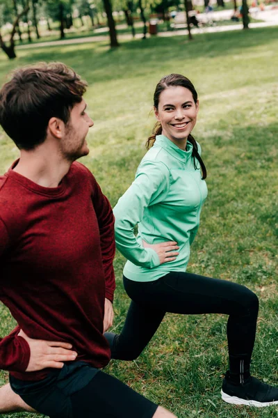 Selektiver Fokus der schönen Frau, die den Mann anlächelt, während sie im Park Ausfallbewegungen macht — Stockfoto