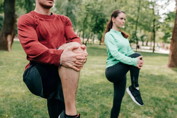 Selective focus of couple stretching legs while working out in park — Stock Photo