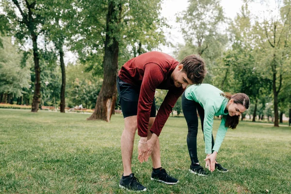 Pareja joven sonriendo mientras se estiran juntos en el parque - foto de stock