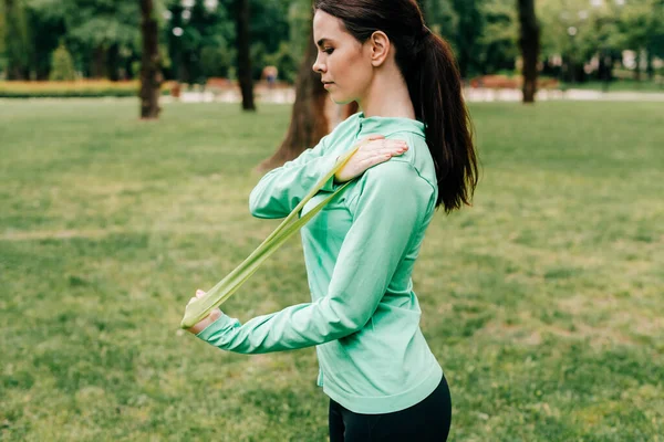 Side view of beautiful sportswoman pulling up resistance band in park — Stock Photo