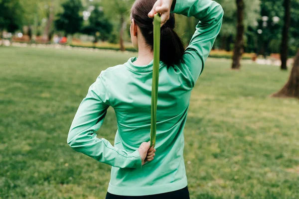 Rückansicht einer Sportlerin, die im Park Widerstandsband hochzieht — Stockfoto