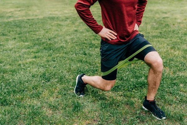 Cropped view of sportsman doing lunges with elastics band in park — Stock Photo