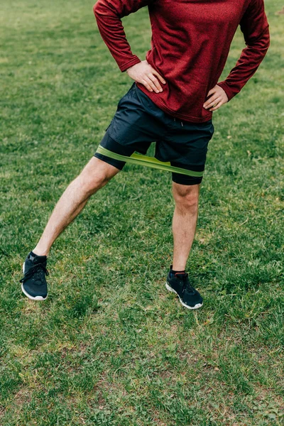 Cropped view of sportsman with hands on hips exercising with elastics band in park — Stock Photo
