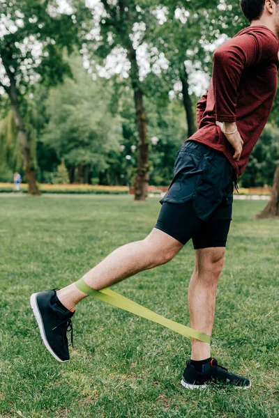 Vista recortada del deportista usando banda elástica mientras entrena en el césped en el parque - foto de stock