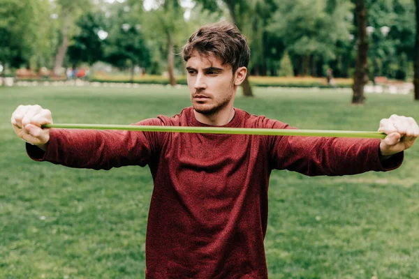 Handsome sportsman pulling up elastics band in park — Stock Photo