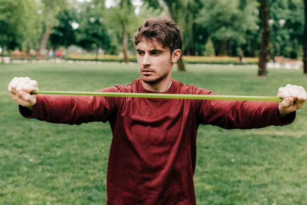 Guapo deportista tirando de banda elástica en el parque - foto de stock