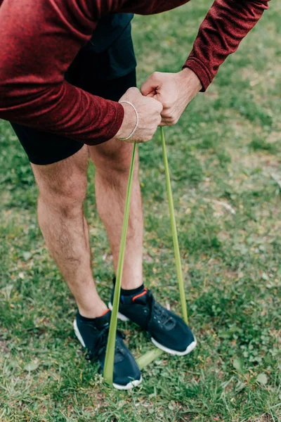 Cropped view of sportsman pulling elastics band while training in park — Stock Photo