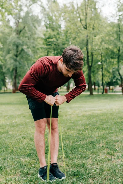 Молодой спортсмен подтягивает пояс сопротивления на газоне в парке — стоковое фото