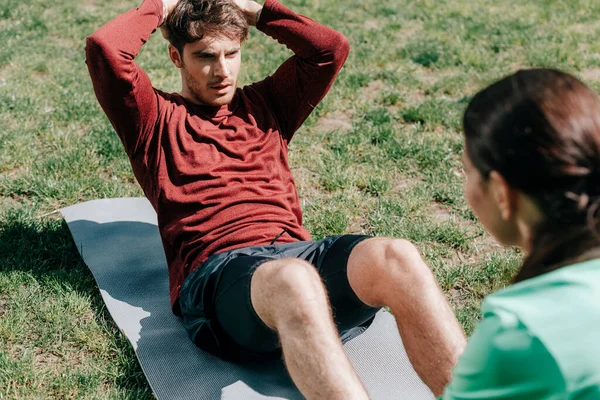 Concentration sélective de bel homme faisant abdos près de petite amie sur tapis de fitness dans le parc — Photo de stock