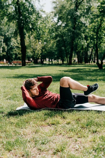 Side view of sportsman doing abs while working out on fitness mat in park — Stock Photo