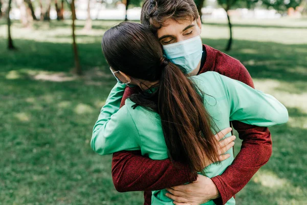 Deportista en máscara médica abrazando a deportista en parque - foto de stock