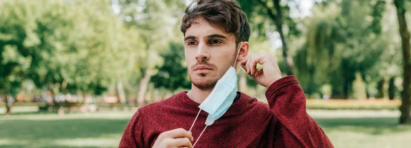 Panoramic shot of sportsman taking off medical mask in park — Stock Photo