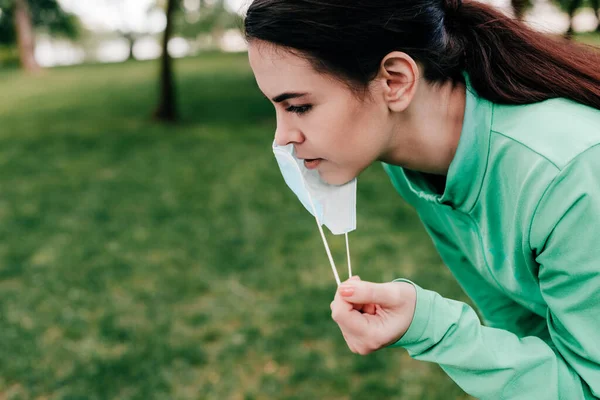 Side view of sportswoman taking off medical mask in park — Stock Photo