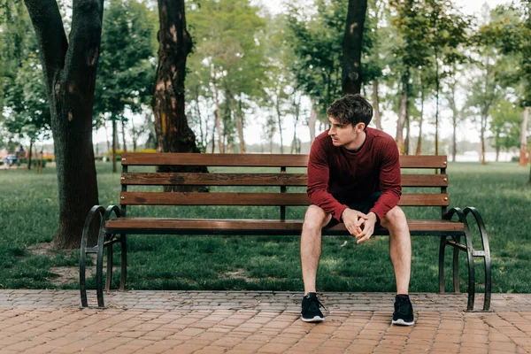 Esportista bonito sentado no banco no parque — Fotografia de Stock