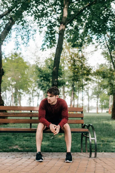 Schöner Mann in Sportbekleidung sitzt auf Bank im Park — Stockfoto