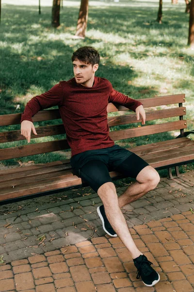 Esportista bonito descansando no banco no parque — Fotografia de Stock