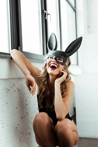 Mujer joven con máscara de conejo riendo cerca de la ventana - foto de stock