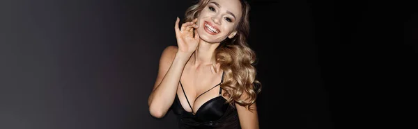 Imagen panorámica de la sensual mujer rubia sonriendo a la cámara aislada en negro - foto de stock