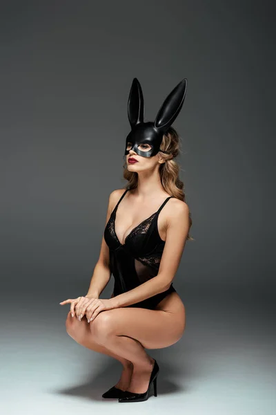Mulher loira sedutora em máscara de coelho e bodysuit em fundo cinza — Fotografia de Stock