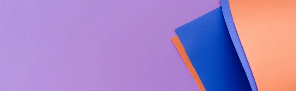 Remolino de papel colorido azul y naranja sobre fondo lila, plano panorámico - foto de stock