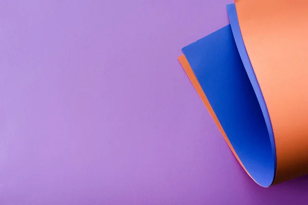 Papier coloré bleu et orange tourbillonnant sur fond lilas — Photo de stock