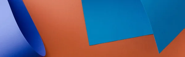 Blaues buntes Papier auf orangefarbenem Hintergrund, Panoramaaufnahme — Stockfoto