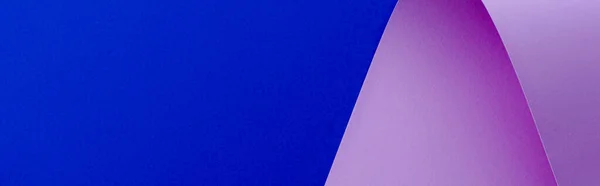 Panoramic shot of curved lilac paper on blue background — Stock Photo