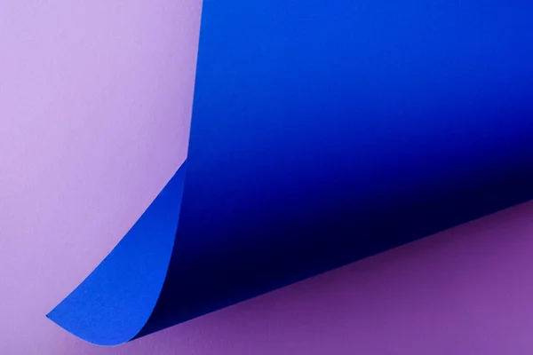 Papel azul curvado sobre fondo violeta - foto de stock