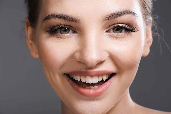Nahaufnahme einer glücklichen jungen Frau mit Make-up, die lächelt und in die Kamera schaut, isoliert auf grau — Stockfoto