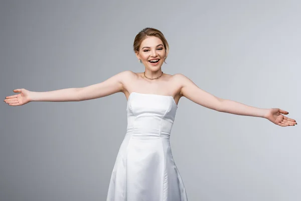 Novia alegre en vestido de novia blanco con las manos extendidas aisladas en gris - foto de stock