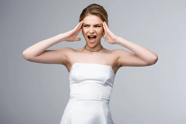 Noiva emocional no vestido de casamento branco tocando templos e gritando isolado no cinza — Fotografia de Stock