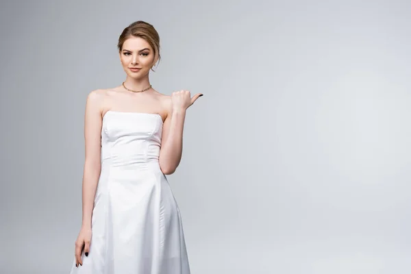 Sposa confusa in abito da sposa bianco punta con pollice isolato su grigio — Foto stock
